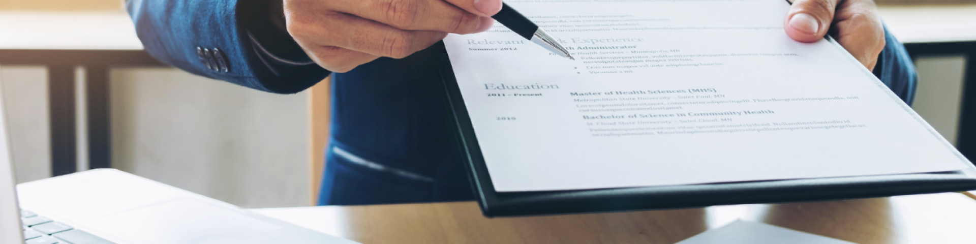 Paper form on a clipboard. There is a hand offering a pen to fill out the paper form.